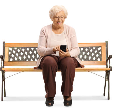 An elderly lady is sitting on a bench using her cell phone and smiling.